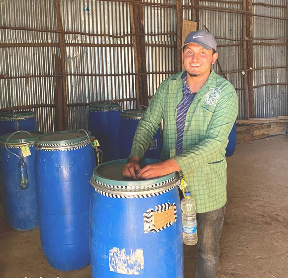 A person standing next to large blue fermentation tanks used for processing coffee, smiling at the camera.