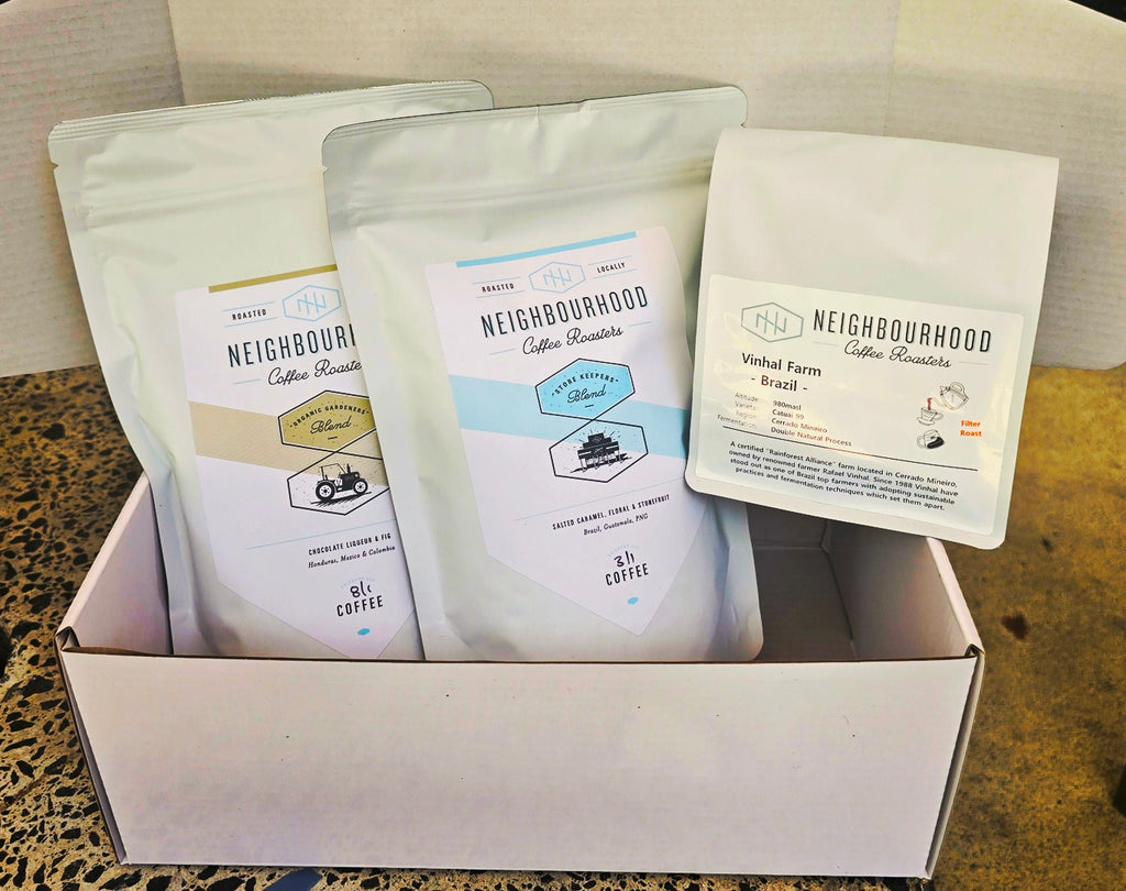 A white gift box containing three bags of coffee, each labeled with different coffee blends such as 'Organic Gardener', 'Store Keepers', and 'Ngororero Farmgate Rwanda'. The bags are displayed in a way that their labels are visible to the viewer.