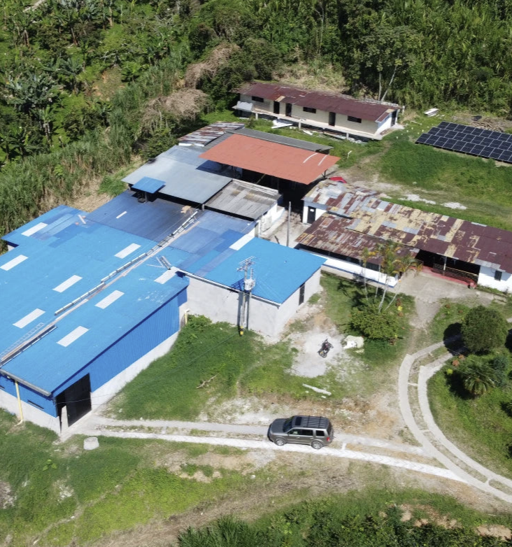 Aerial view of a building complex with blue roofs and solar panels in a forested area.