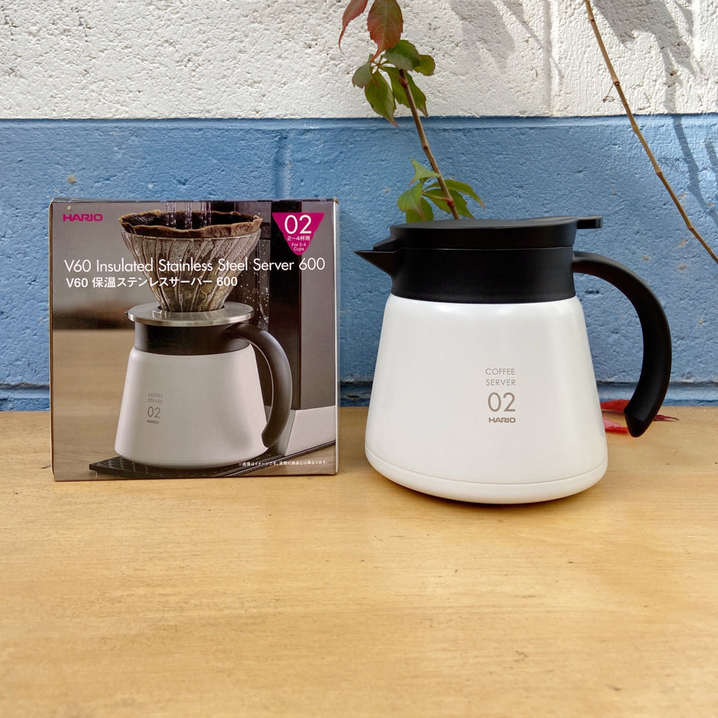 A white Hario V60 insulated stainless steel coffee server with a lid, next to its packaging box with Japanese text.