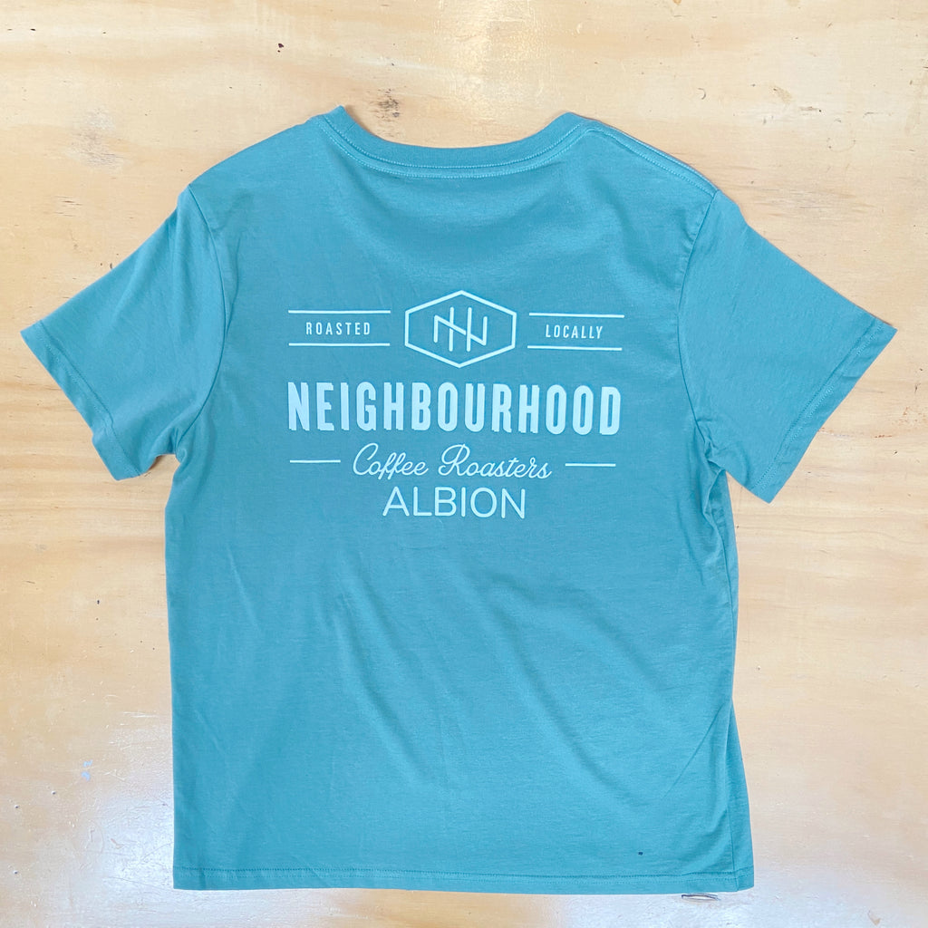 A green t-shirt with text and logo related to a coffee roasters brand, placed on a wooden surface.