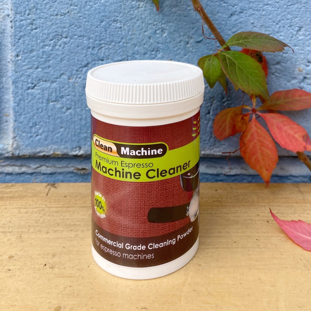 A container of Clean Machine Premium Powder for commercial and domestic machines, placed against a backdrop featuring a blue wall and red flowers.