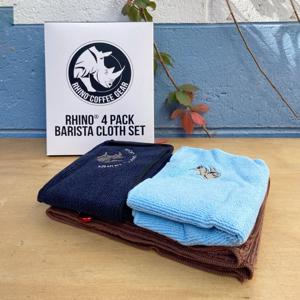 A set of three microfiber coffee cleaning cloths in brown, blue, and black, with the Rhino Coffee Gear logo, displayed on a wooden surface with a branded packaging in the background.