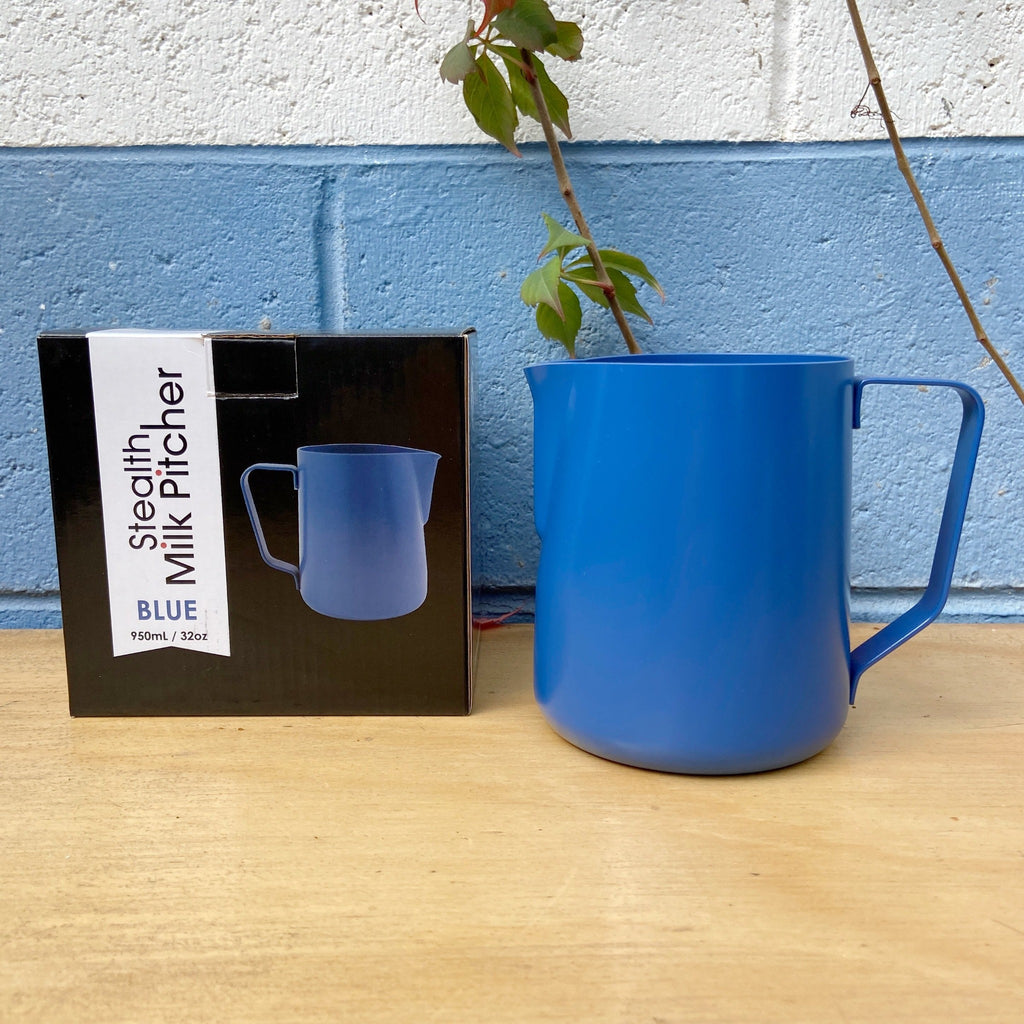 A blue 950ml Rhino Stealth Milk Jug with a black pitcher, placed next to its packaging box with a plant in the background.