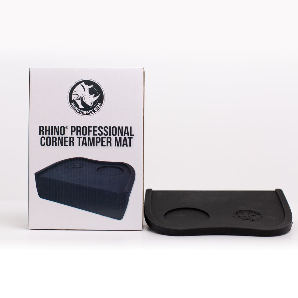 A black Rhinowares Professional Corner Tamper Mat placed in front of its packaging box with the product name visible.