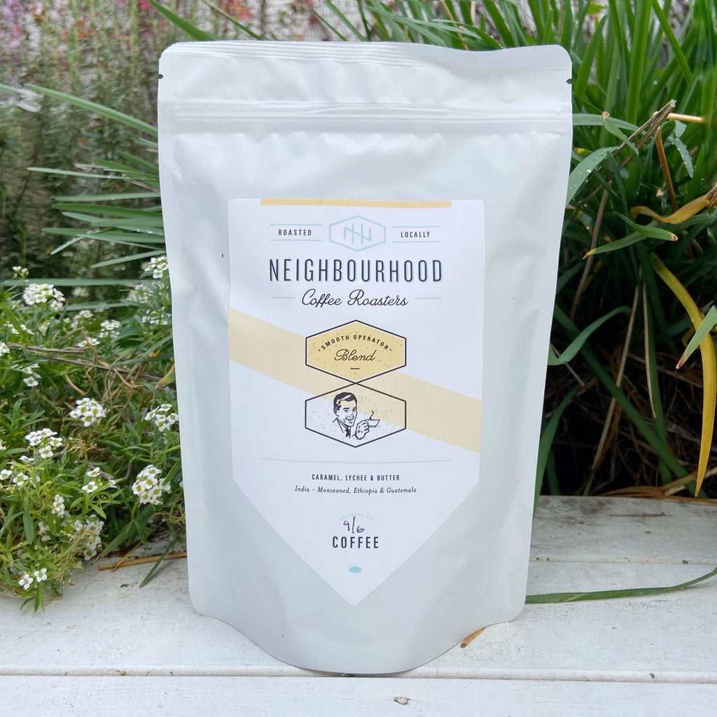 A packaged bag of Neighbourhood Coffee Roasters coffee blend, Smooth Operator, displayed in front of a greenery background.