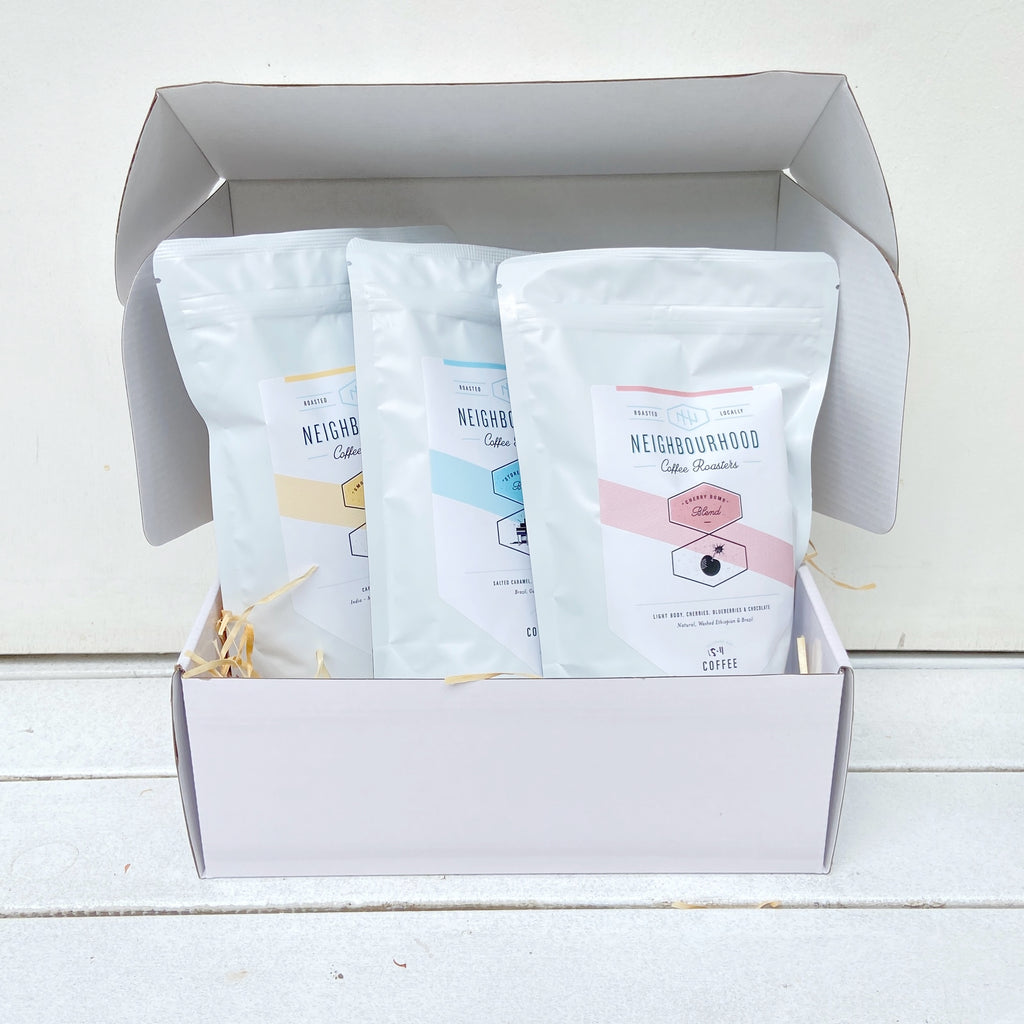 A white glossy gift box open to reveal three individual coffee bag packages labeled Cherry Bomb, Store Keepers, and Smooth Operator.