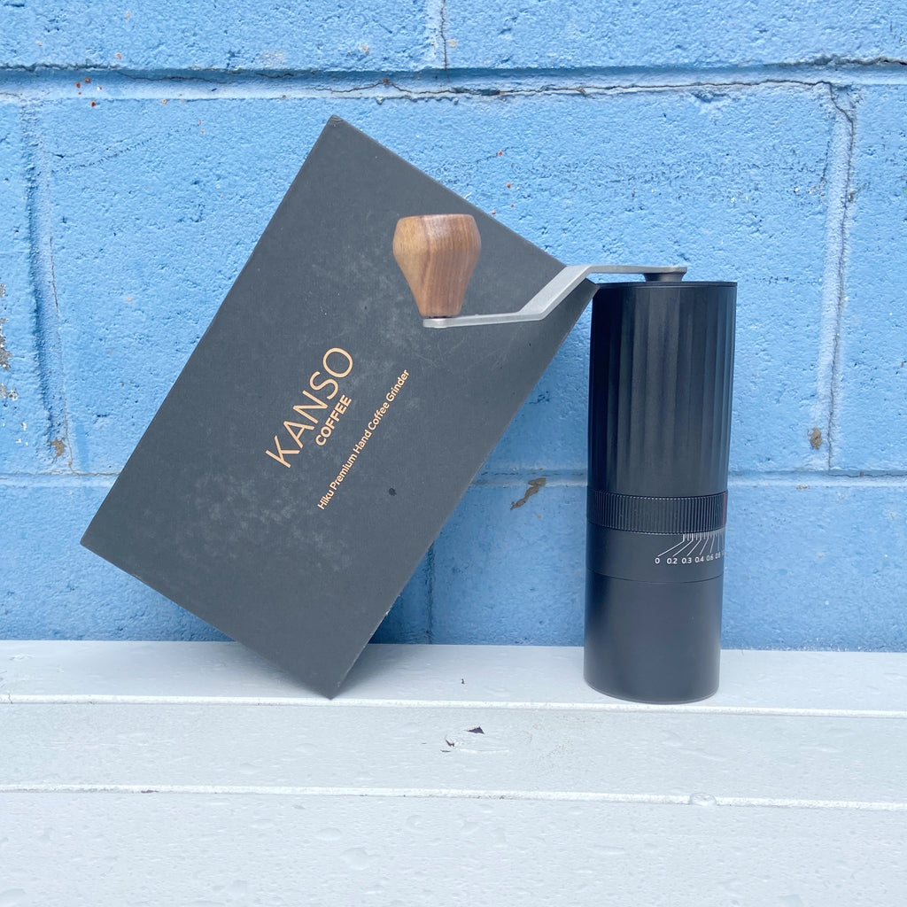 Kanso Hiku Hand Coffee Grinder with a black body, a walnut knob on the top, and a blue background.